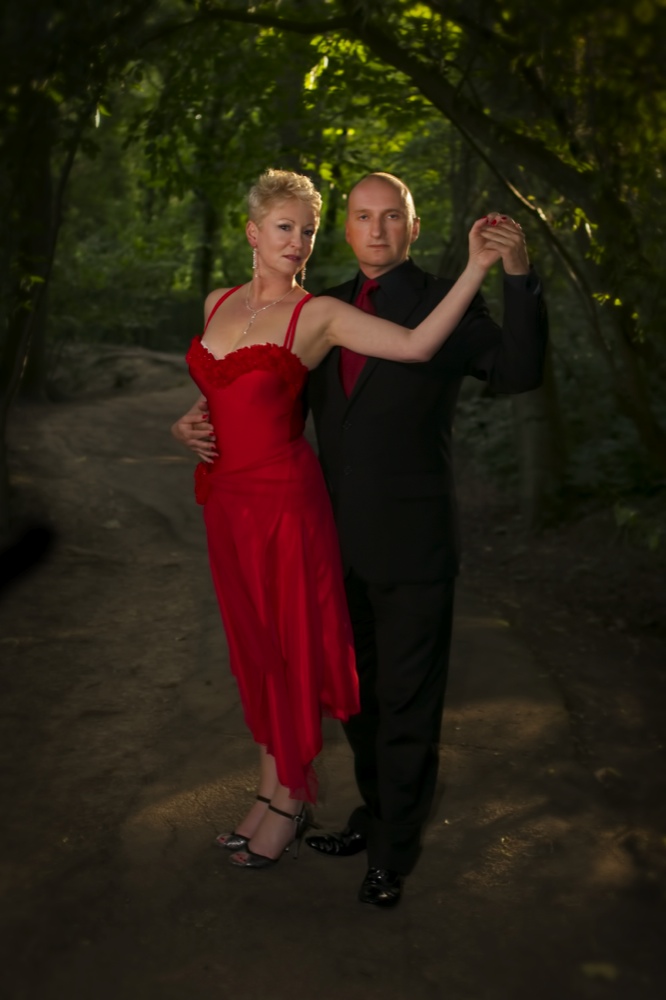 David and Ann in a formal tango embrace on a woodland path, looking toward the camera
