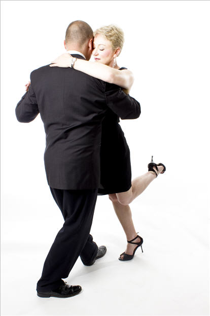 David and Ann in a close tango embrace, Ann's leg flicking up, white studio backdrop